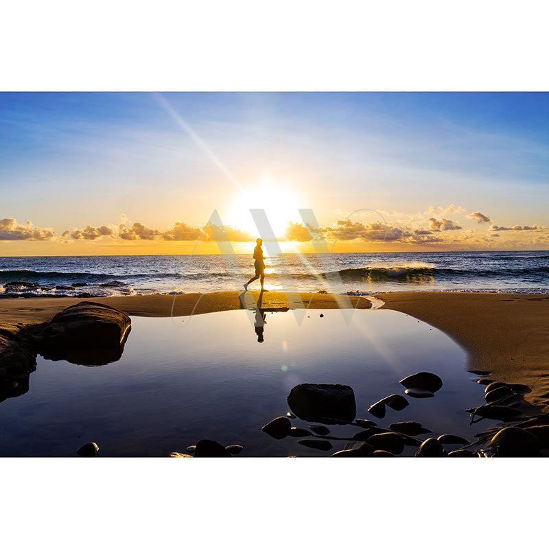 A silhouette of a person carrying a surfboard walks along the beach at sunset, with colorful skies, ocean waves, and kite surfers in the background.