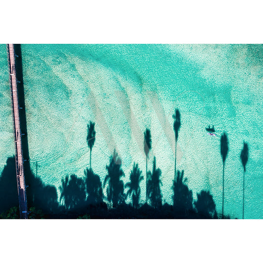 Brunswick Heads Drone Image 0195 from AWP Image Library captures an aerial view of turquoise waters with dark palm tree silhouettes casting shadows, a small boat in the upper right corner, and a wooden pier along the left side of the frame.