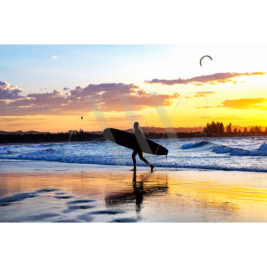 Byron Bay Surfer Image 5977 by AWP Image Library features a person silhouette with a surfboard walking along the shore at sunset, under a vibrant orange and yellow sky as gentle waves lap the beach.