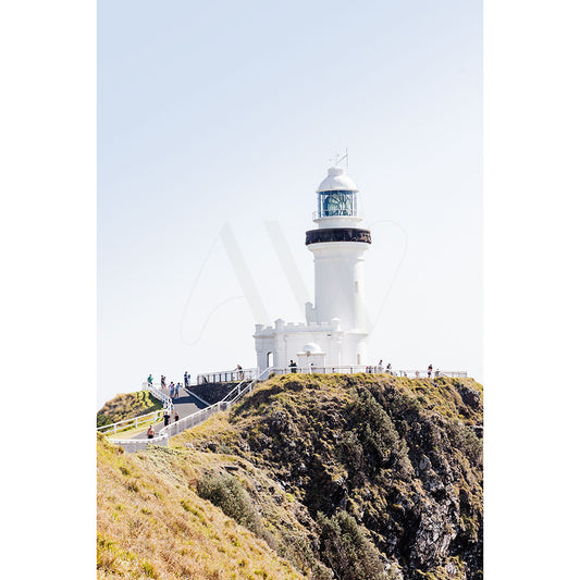 A white lighthouse from AWP Image Librarys Byron Bay Template stands tall on a grassy cliff under a clear blue sky where people stroll along a path, savoring the scenic view.