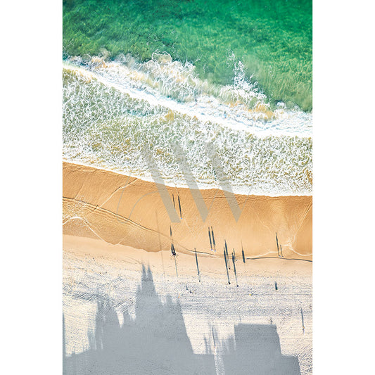 The Caloundra Drone Image 0352 by AWP Image Library captures an aerial view of a sandy beach with turquoise waves, where shadows from a large building and individuals create a striking contrast against the bright shoreline.