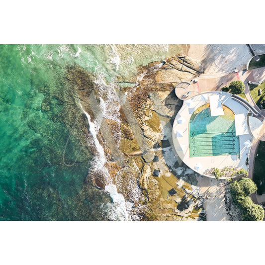 The Caloundra Kings Beach Image 0205 by AWP Image Library showcases an aerial view of an ocean pool encircled by rocks and clear green-blue water, with lanes and a promenade, as sunlight casts shadows of trees and structures.