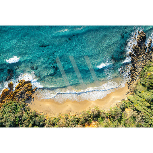 The Coolum Beach Drone Image from AWP Image Library captures an aerial view of a secluded beach with golden sand, turquoise waters, gentle waves, rugged cliffs, and lush green foliage in a serene natural setting.