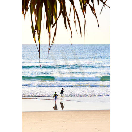 Two individuals stroll along a tranquil shoreline in Coolum Beach Image 9191 by AWP Image Library, where gentle waves touch the sands. The vast ocean stretches to the horizon beneath a clear sky, with palm leaves framing the scene.