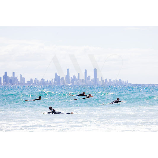 Surfers paddle into the ocean with a city skyline backdrop beneath a clear sky in Currumbin Beach Image 4496 by AWP Image Library.