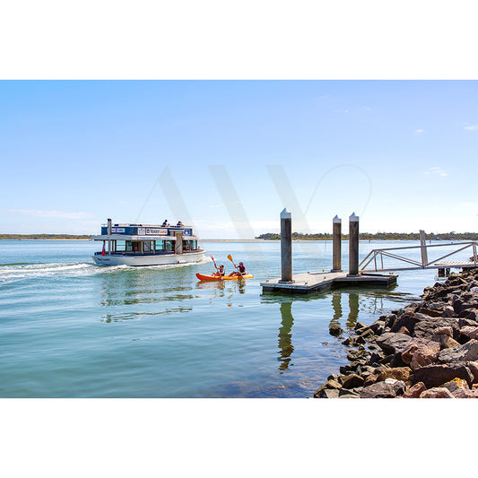 The Gympie Tce Image 8293 from AWP Image Library depicts a small ferry and two people in a kayak on calm water near a dock, under a clear bright sky with rocks lining the shore.