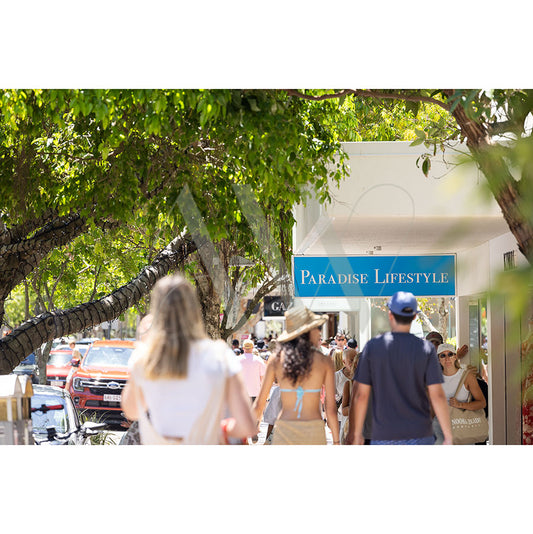 Individuals stroll along a tree-lined street under a blue sign labeled Paradise Lifestyle in the Hastings Street Image 4962 from AWP Image Library.