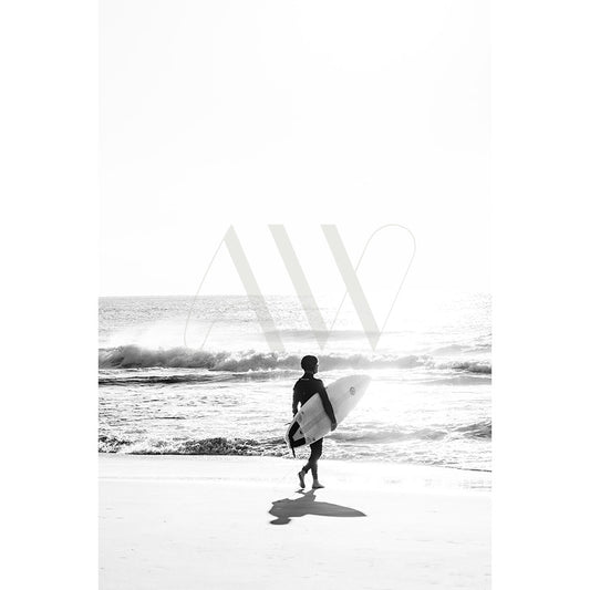 The Lone Surfer BW Image 8722 from AWP Image Library captures a solitary surfer with a surfboard walking along the beach towards the sea, against a backdrop of crashing waves and a bright sky, evoking serenity and adventure in black and white.