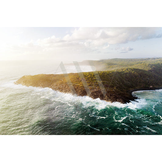 Capture the stunning Noosa River Drone Image 0855 from AWP Image Library, showcasing the rugged coastline of Noosa National Park. Experience waves crashing on rocky shores, lush green landscapes, and a partly cloudy sky basked in warm sunlight for an enchanting view.