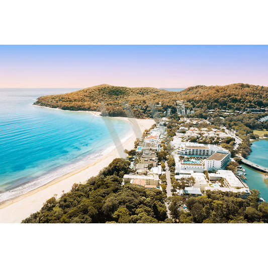 Product Description: The Noosa Main Beach Drone Image 253 by AWP Image Library captures an aerial view of a coastal town with sandy beaches, clear waters, and lush hills. Buildings cluster near Hastings Street by Noosas Main Beach as the ocean extends under a pastel morning sky.