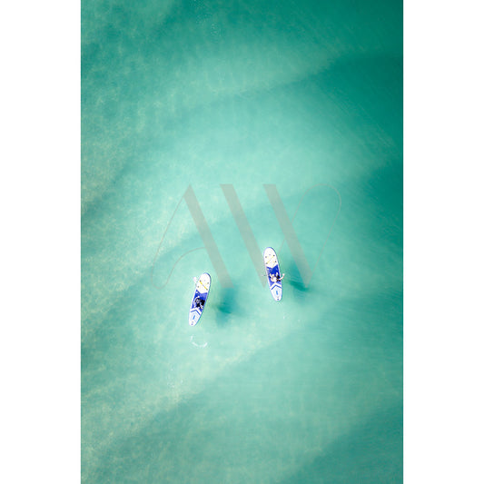 The Noosa River Drone Image 0947 from AWP Image Library captures two people paddleboarding on clear turquoise water, creating ripple patterns. The boards are arranged diagonally, with sunlight casting subtle shadows on the waters surface.