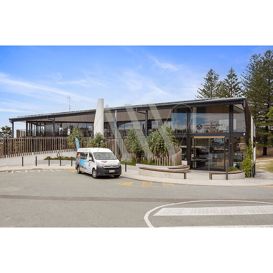 The Sunshine Beach Surf Club 2520, by AWP Image Library, features a modern design with large glass windows and a right-side canopy. A small van is parked in front on the left, surrounded by trees under a clear blue sky.