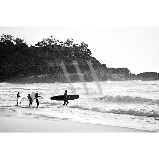 A black and white image from AWP Image Librarys Product template shows five people with surfboards heading into the ocean, set against a sandy beach with rocky cliffs and trees.